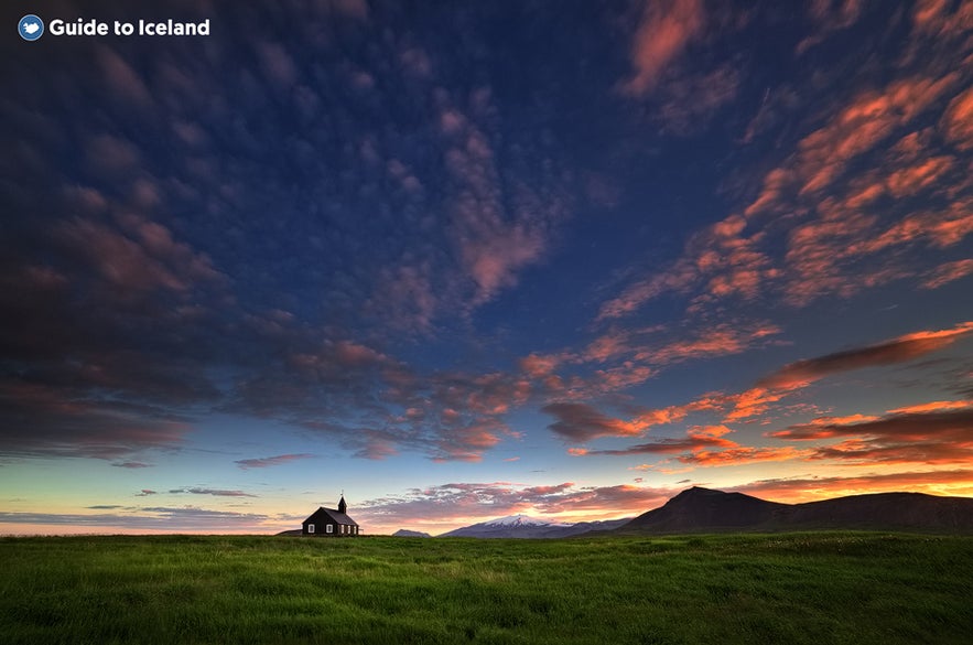 The black Budakirkja church during a sunset, with the sky and the mountains as its backdrop.