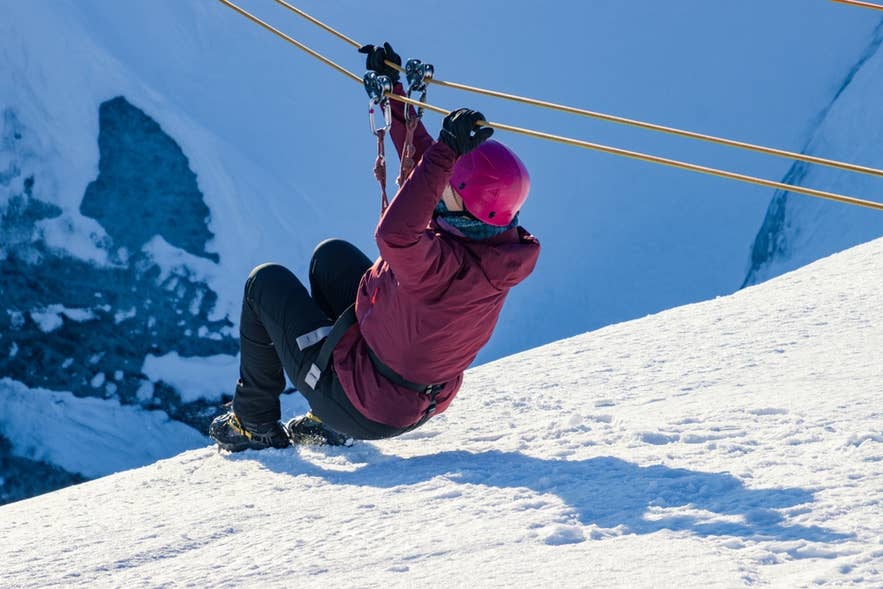 A zipliner in a red jacket rides above a glacier crevasse, one of the most extreme activities in Iceland.