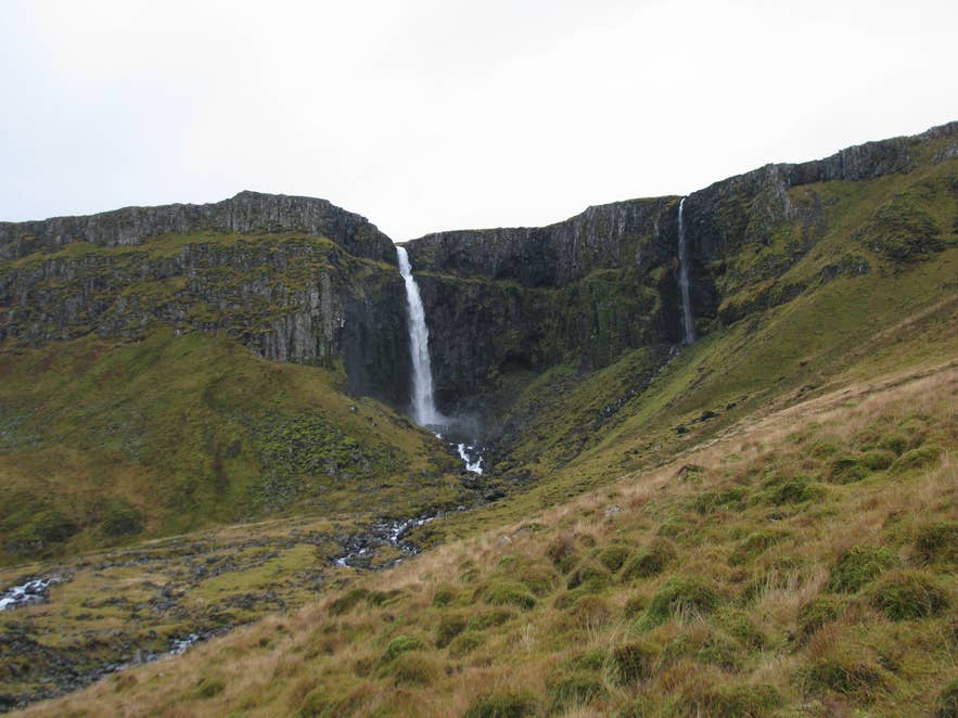 Grundarfoss Waterfall drops from a green cliff into a rocky amphitheater east of Grundarfjordur.