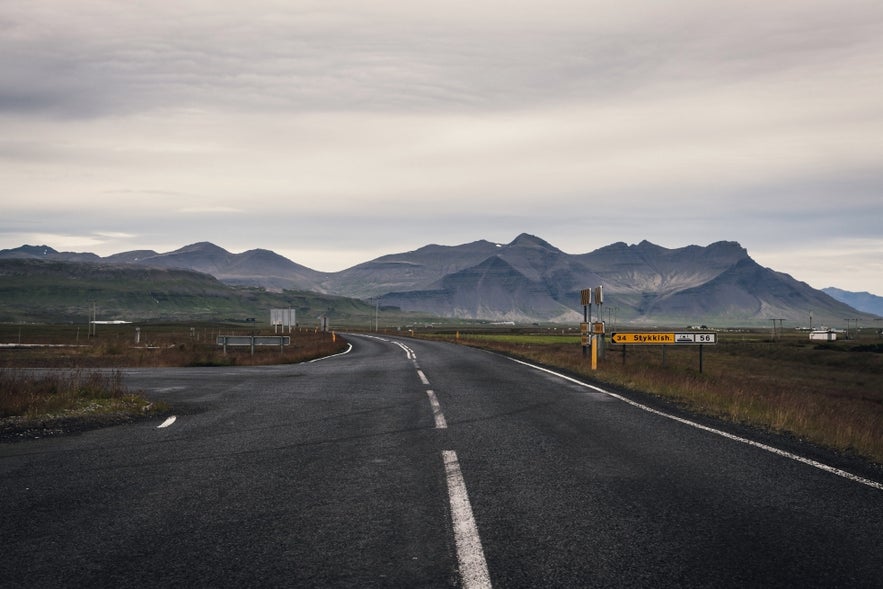An empty road with a yellow Icelandic road sign pointing to Stykkisholmur in West Iceland.