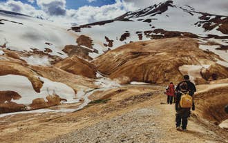 Vandrere går gennem den geotermiske dal Hveradalir i Kerlingarfjöll med dampende sprækker, røde bakker og pletter af sommersne.