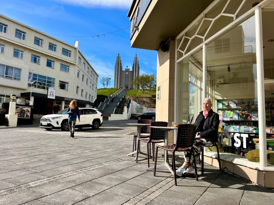 Woman sitting outside at LYST in Penninn Eymundsson bookstore in Akureyri, with Akureyrarkirkja in the background.