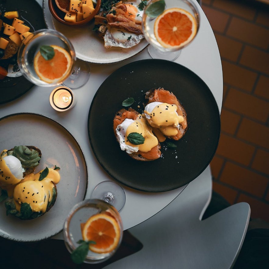 Overhead view of a brunch spread with salmon eggs benedict, avocado toast with poached egg, fruit salad, and drinks at Ketilkaffi in Akureyri.