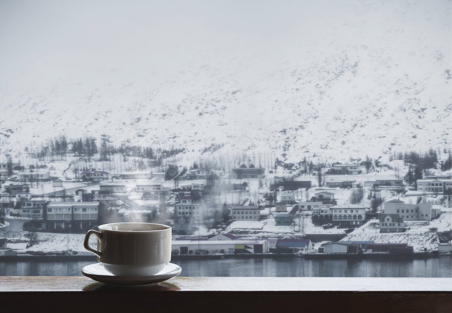 A steaming cup of coffee or tea with a snowy town and mountain view in Akureyri.