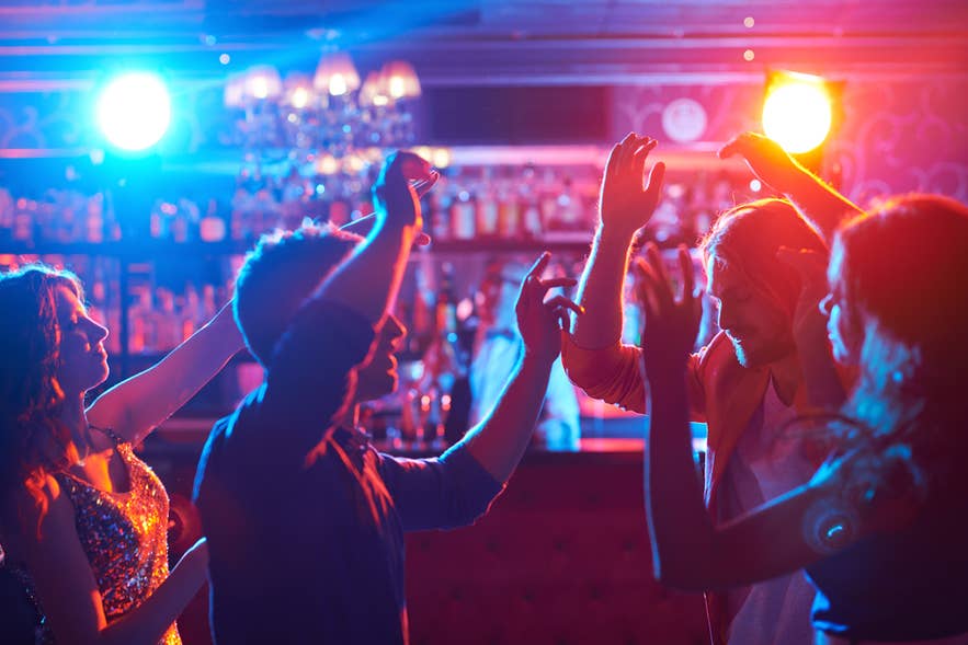 Uitgaanspubliek danst onder kleurrijke podiumverlichting in een nachtclub in Reykjavik na middernacht.