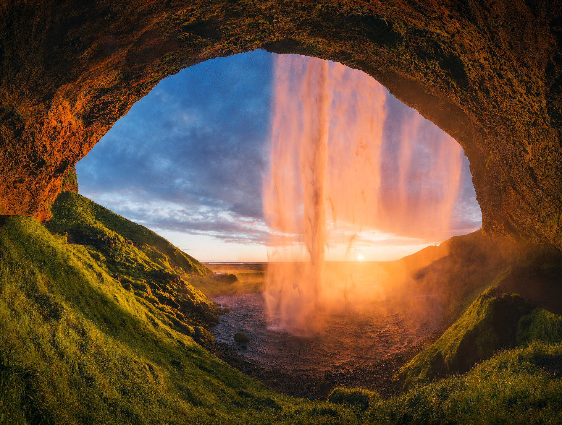 Der Seljalandsfoss leuchtet im warmen Licht der untergehenden Sonne – betrachtet von der Höhle aus, hinter dem herabstürzenden Wasserfall.