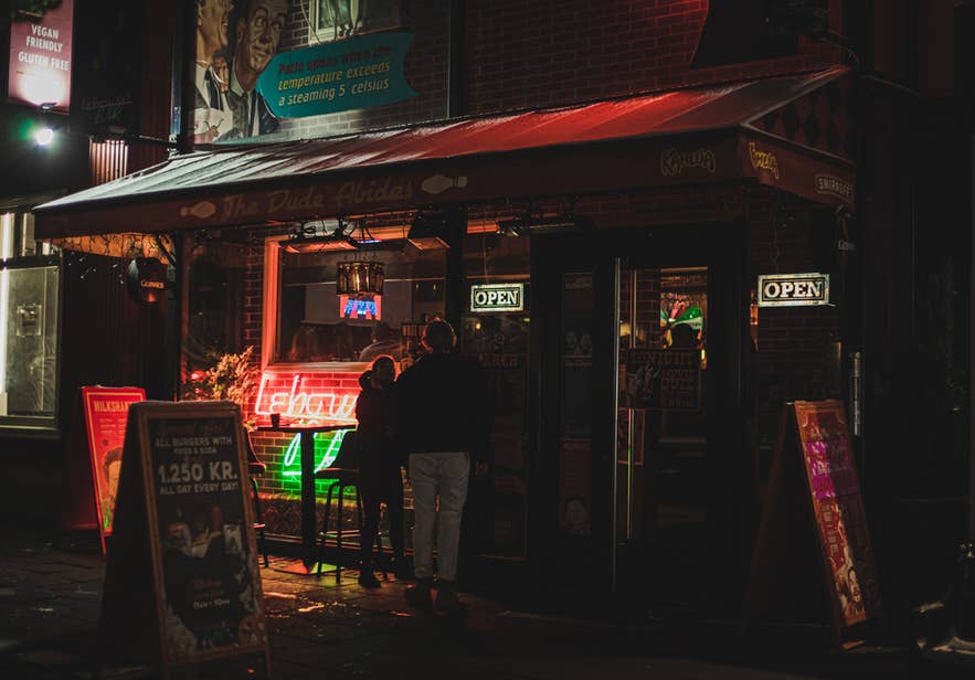 Straatkraam met laatavondeten in het centrum van Reykjavik, met neonborden waarop staat dat de zaak geopend is en een kleine menigte.