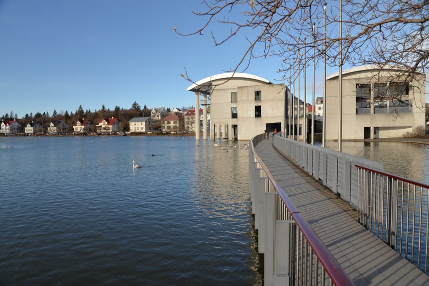 Pedestrian bridge over Tjornin Pond leading to Reykjavik City Hall, with swans on the water in downtown Reykjavik