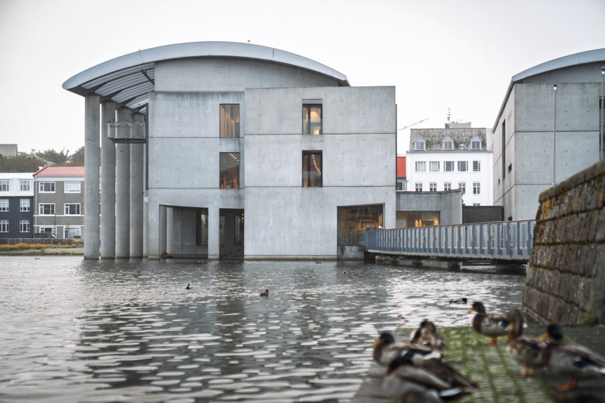 Reykjavik City Hall seen from Tjornin Pond with modern concrete facade, water reflections, and ducks in the foreground