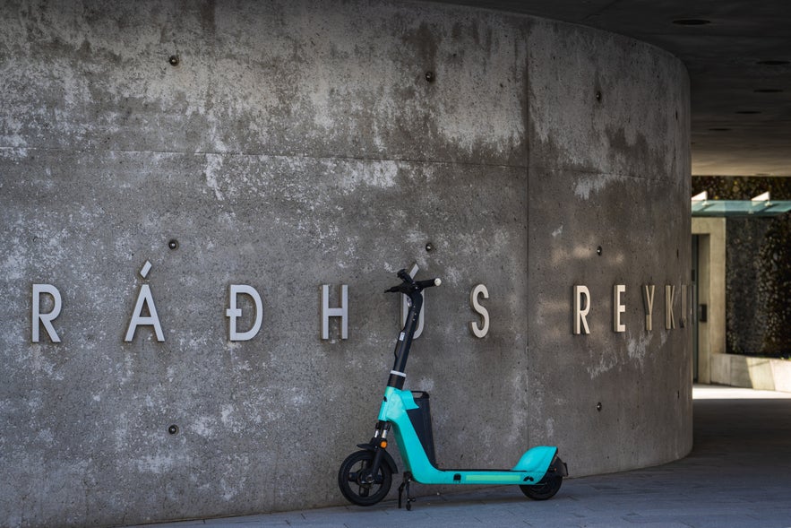 Electric scooter parked outside Reykjavik City Hall, with R&aacute;&eth;h&uacute;s Reykjav&iacute;kur signage on the concrete exterior wall