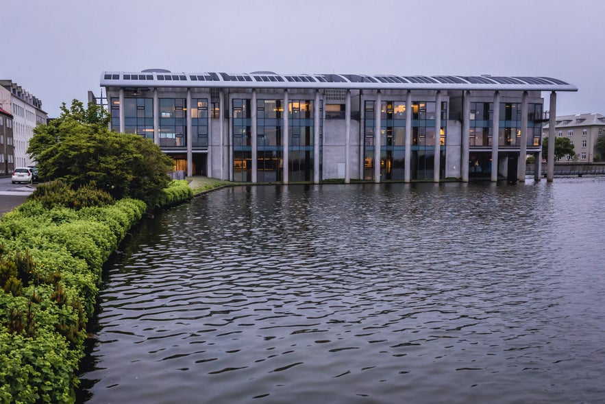 Reykjavik City Hall viewed across Tjornin Pond, highlighting its modern concrete columns and glass facade at dusk