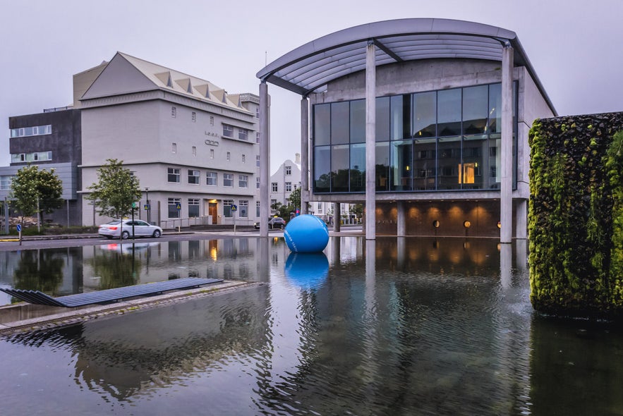 Reykjavik City Hall reflected in Tjornin Pond, showing modern glass facade and outdoor art installation in downtown Reykjavik