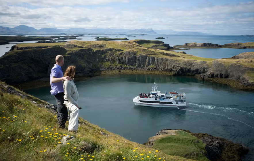 Couple watching a sightseeing boat cruise through Breidafjordur Bay in Iceland.