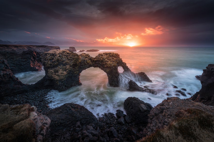 Natural stone arch on the Arnarstapi coast at sunset in Iceland.