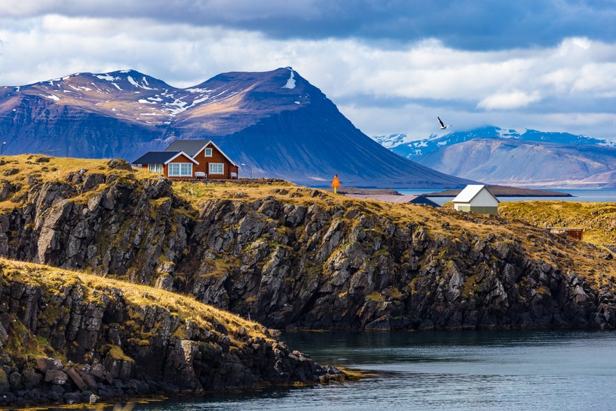 Scenic view of Arnarstapi village with rugged shoreline and dramatic peak.