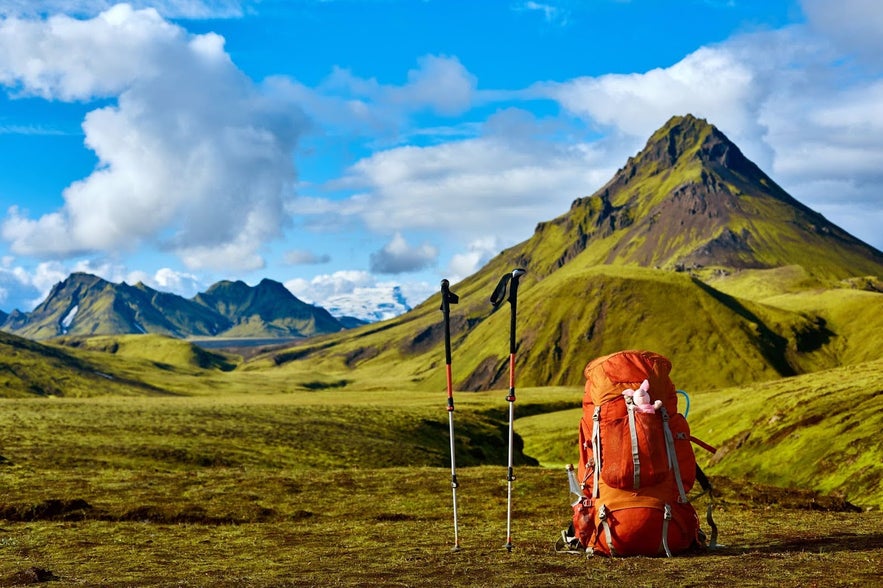 Backpack and trekking poles in front of a green volcanic mountain in Iceland.