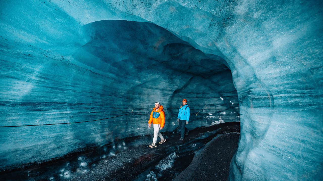 Deux personnes explorent la grotte de glace bleue de Katla, équipées de casques et de vêtements d'hiver à l'intérieur du glacier.