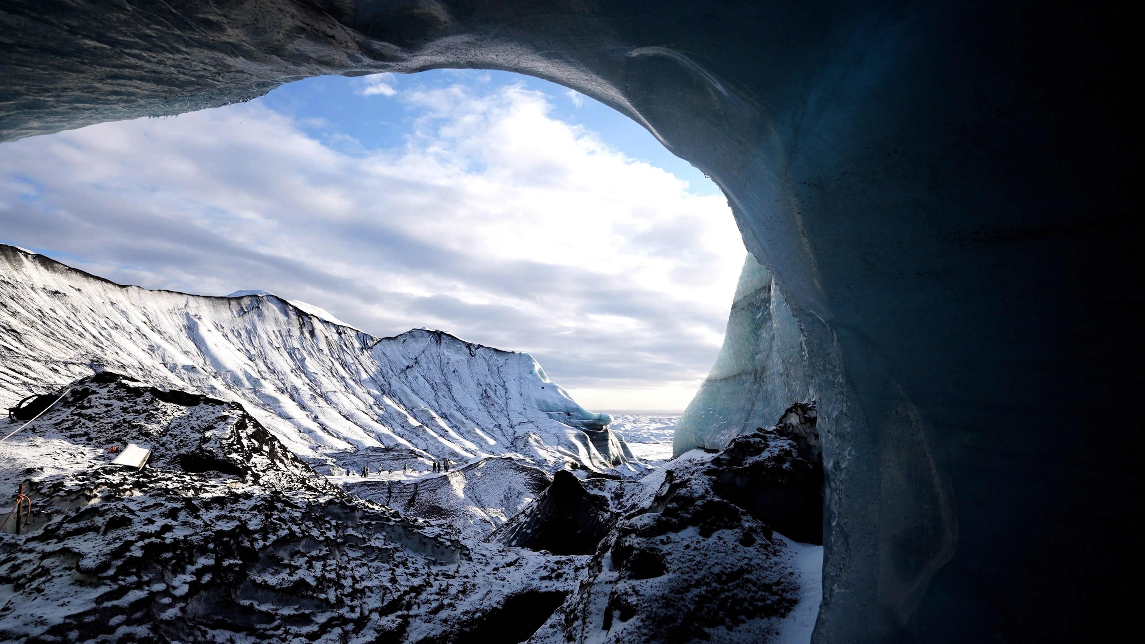 View from inside the Katla Ice Cave overlooking snow-covered volcanic peaks under a cloudy sky.