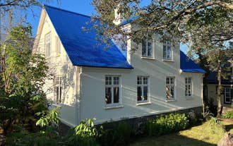: Luxury Villa Downtown Reykjavik with a bright blue roof, cream walls, and surrounded by trees and garden.