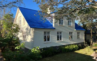 : Luxury Villa Downtown Reykjavik with a bright blue roof, cream walls, and surrounded by trees and garden.