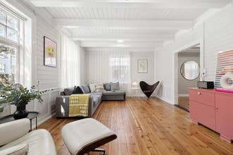 Salón espacioso con gran sofá gris en L, suelo de madera y paredes blancas con paneles.