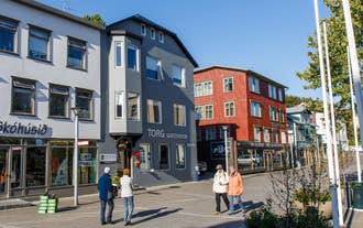 Torg Guest House on Akureyri town square with people walking past shops and colorful buildings nearby.