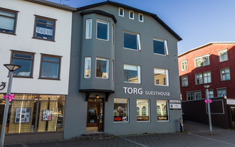Front view of Torg Guest House in Akureyri with a gray facade and large windows facing the town square.