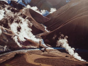 Aerial view of geothermal steam vents and hiking trails in Hveradalir valley, surrounded by red rhyolite hills and winding rivers