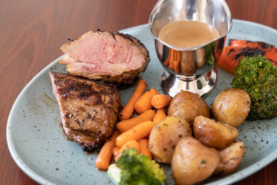 Grilled lamb with sauce, broccoli, potatoes, and carrots.