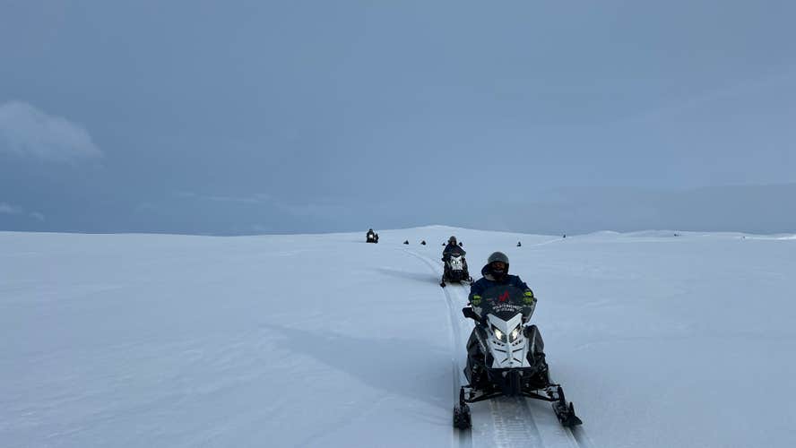 A group rides snowmobiles across Langjokull Glacier during a guided Iceland snowmobile tour.