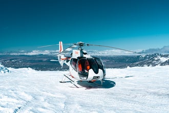 White helicopter with red markings lands on snowy Langjokull Glacier with mountains stretching in the distance.