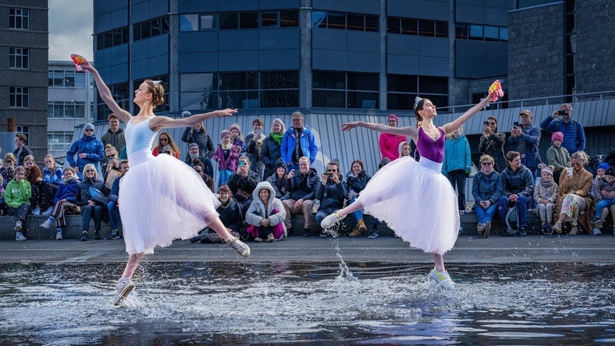 Two ballet dancers perform in colorful tutus and sneakers on a water-covered stage during Culture Night in Reykjavik, Iceland, with a captivated audience watching in the background.