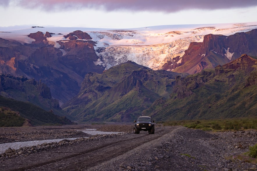A 4x4 vehicle drives on a gravel road with Eyjafjallajökull glacier-covered volcano in the background during sunset.