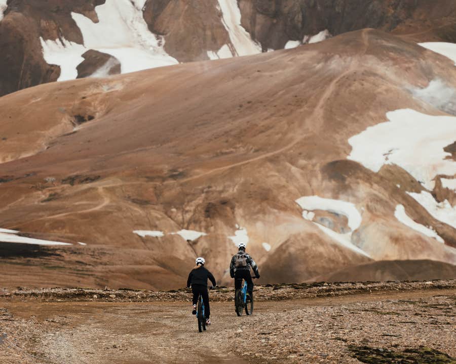 Deux cyclistes traversent les montagnes enneigées des Hautes Terres en Islande.