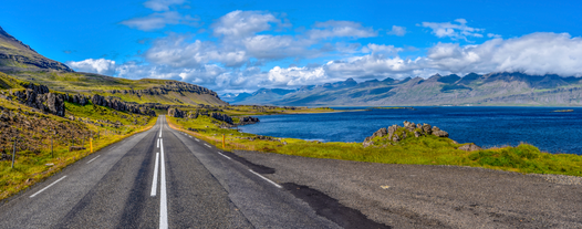 Ring Road 1 in East Iceland with a view of Stöðvarfjörður fjord and distant mountains under a clear blue sky.