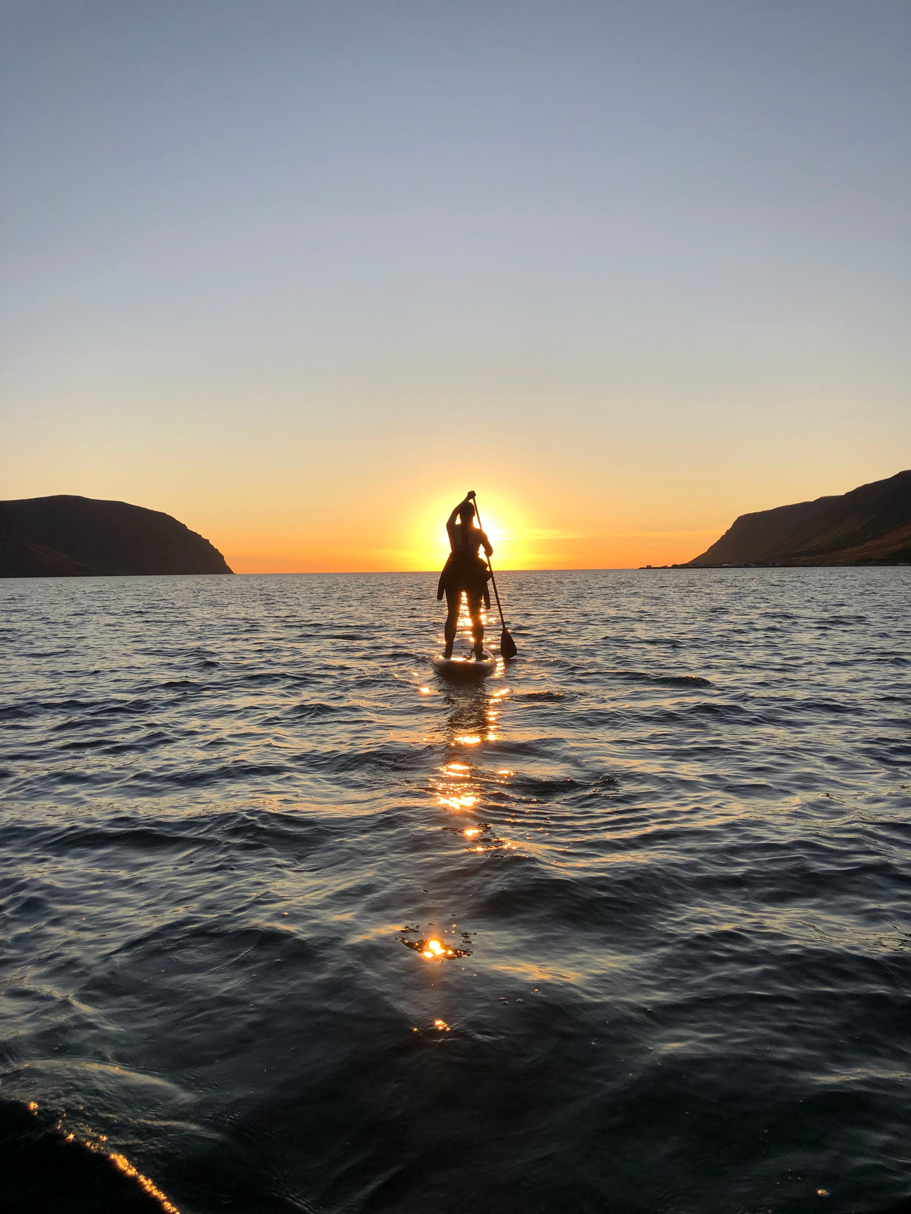 Iceland paddleboarding at sunset with a silhouette against golden water in the Westfjords.