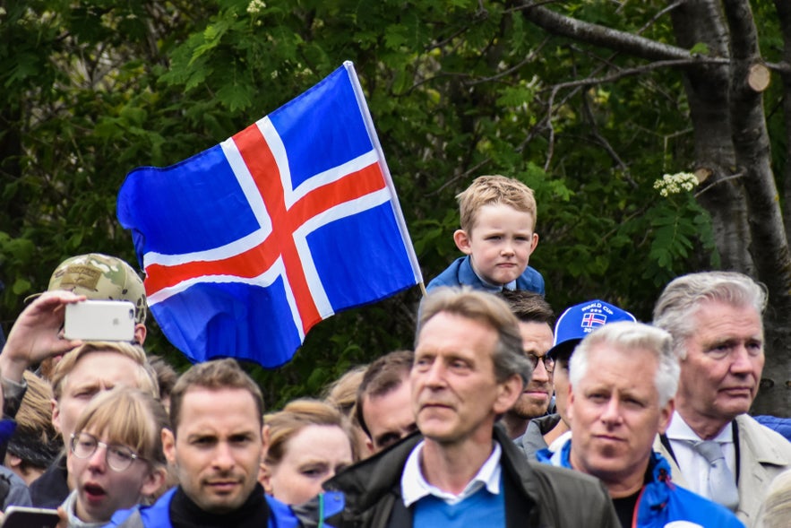 Crowd celebrating Iceland's National Day at Austurvöllur Square in Reykjavik with Icelandic flag and families in view.