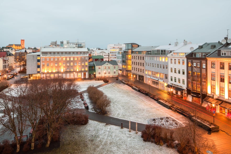 Austurvöllur Square in Reykjavik on a winter evening, surrounded by lit buildings and light snow on the ground.