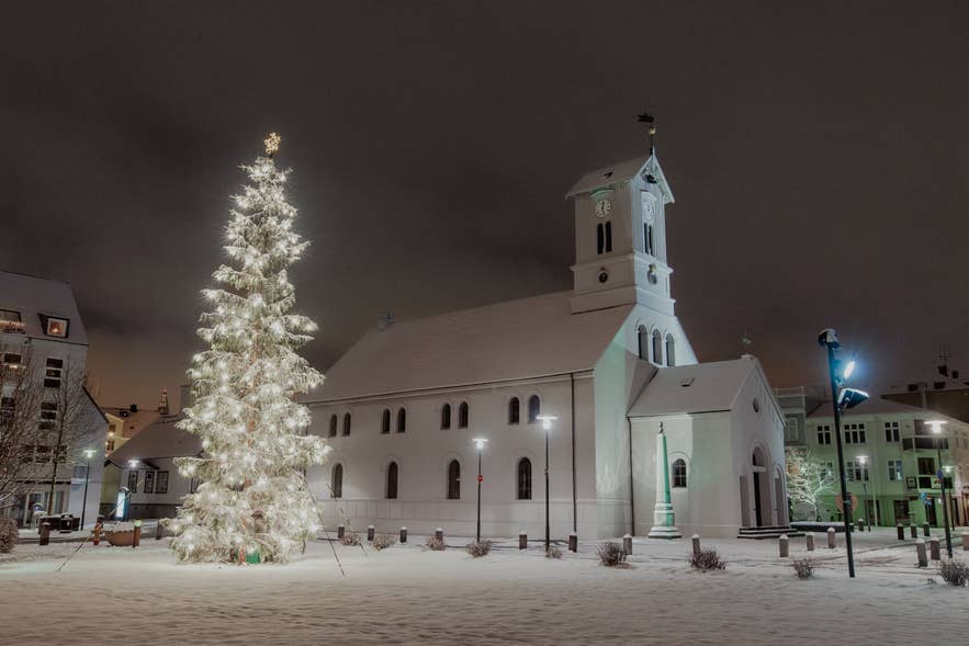雪の夜、オーストゥルヴォットル広場のレイキャビク大聖堂と輝くクリスマスツリー。