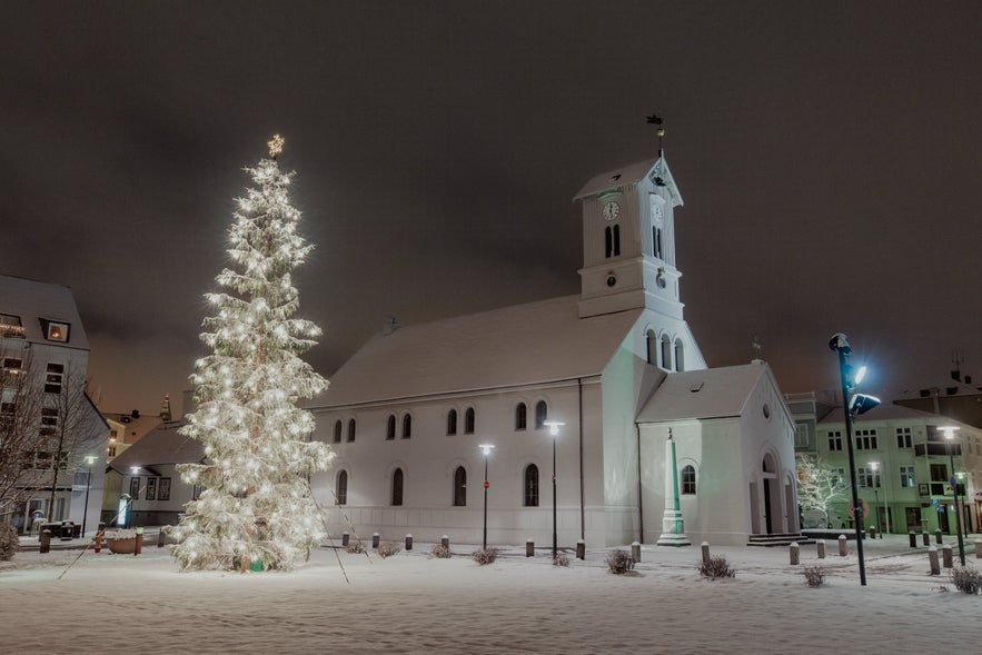 Reykjavik Cathedral and a glowing Christmas tree at Austurvöllur Square on a snowy winter night.