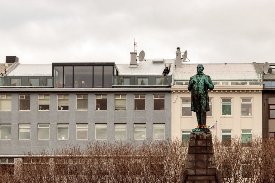Jón Sigurðsson statue at Austurvöllur Square in Reykjavik, Iceland, with modern buildings and bare winter trees in the background.