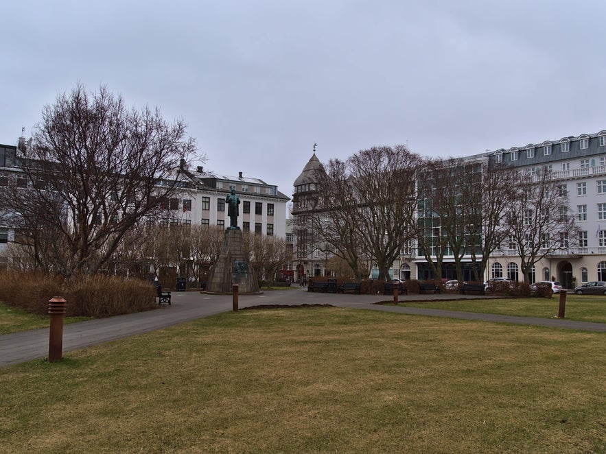 View of Austurvöllur Square in Reykjavik with the Jón Sigurðsson statue, bare trees, and surrounding historic buildings.