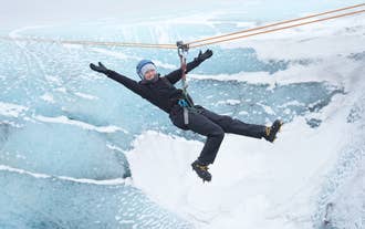 A woman strapped to a zipline poses happily for a photo mid-air, one of the best things to do in  the South Coast.