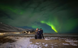 A family of four, including two adults and two children, stands together under the vibrant green and purple hues of the northern lights.