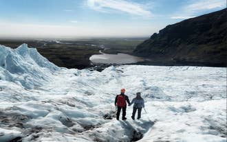A couple holds hands as they walk together, hiking across an icy glacier.