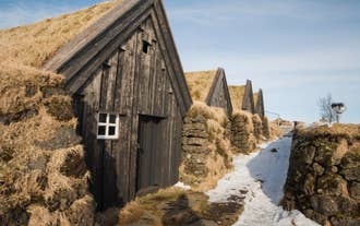 A row of traditional Icelandic turf houses sits alongside a snowy path under a clear sky.