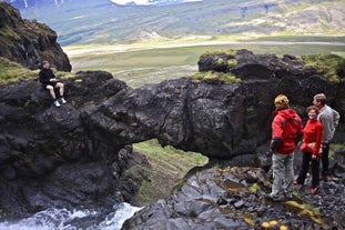 Hiker standing on a natural stone arch over crashing waves at Gatklettur, Arnarstapi.