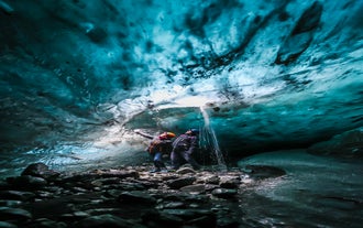 Two travelers framed by deep blue ice formations inside Iceland’s famous glacier cave.