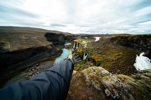 A person holds their hand out in front of mesmerizing cascades in a deep valley.