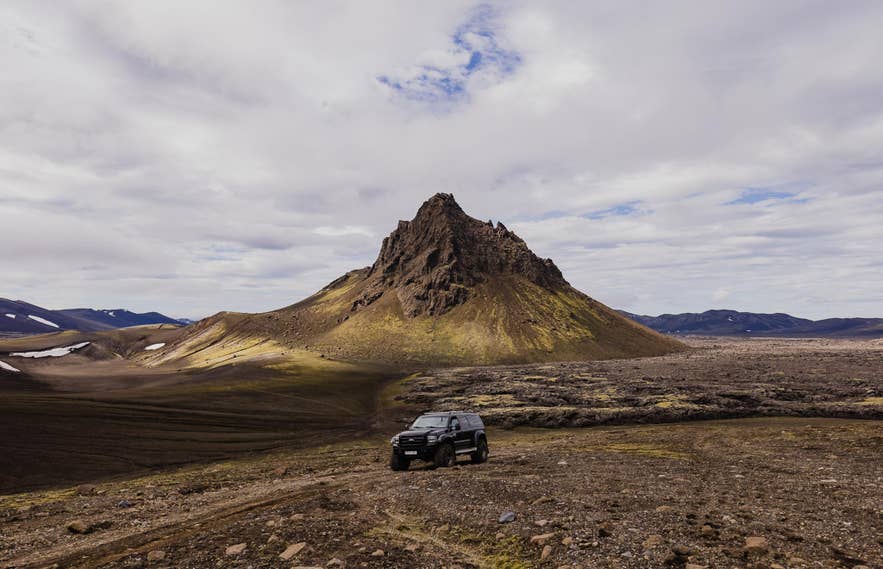 Rental 4x4 navigating a rugged gravel road through Icelandic scenery.
